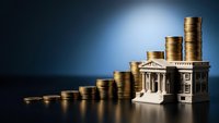 Golden coins stacked in ascending rows leading to miniature bank building on dark blue background representing financial growth and banking services.