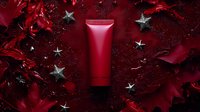 Red cosmetic tube on dark background with silver stars and flowing fabric creates luxurious beauty product presentation for advertising and marketing campaigns.