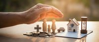 Hand protecting miniature family, house, car and money symbols representing comprehensive life insurance coverage and financial security planning.