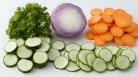 Fresh sliced vegetables arranged in rows including parsley, cucumber rounds, red onion rings and carrot circles on white background, ready for cooking or salad.