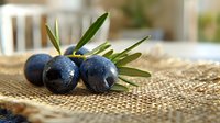 Fresh ripe black olives with green leaves on burlap background, macro shot with selective focus. Natural organic Mediterranean food styling.
