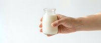 Hand holding glass bottle of fresh milk isolated on white background, suitable for dairy product advertising and nutrition content.