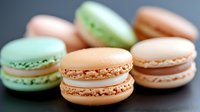 Colorful French macarons in pastel shades of pink, green and peach arranged on dark surface. Sweet confectionery treats for bakery, dessert menu or cafe branding.
