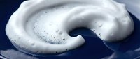 White foamy soap bubbles swirling in circular motion against dark blue background creating cleaning and hygiene concept for household products.