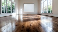 Empty bright room with large windows, sunlight casting shadows on polished hardwood flooring, and blank white canvas on wall, showcasing modern minimalist interior design.