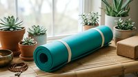 Teal yoga mat rolled up with cork block and succulents on wooden floor near bright window creating peaceful home workout space for meditation and fitness.