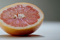 Fresh cut pink grapefruit half showing juicy pulp and segments on white surface with soft focus background, macro food photography.