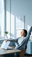 Young woman stretching at desk in bright office with laptop, taking break from work, wellness and productivity concept for remote working lifestyle.