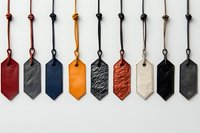 Collection of colorful leather tags or keychains in various shapes and colors including red, blue, yellow, black, and white, hanging on cords against white background.