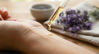 Lavender essential oil dropping from glass dropper onto hand for natural skincare and aromatherapy wellness treatment with dried flowers.
