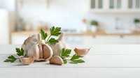 Fresh garlic bulbs and cloves with green parsley leaves arranged on white kitchen counter for cooking and culinary preparation in modern home interior.