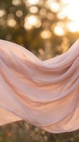 Flowing pink chiffon fabric dancing in golden sunset light with dreamy bokeh background for romantic wedding and fashion concepts.