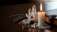 Mystical altar setup with burning candle, crystal quartz points, lavender sprigs and pentagram pendant for spiritual meditation and witchcraft rituals.