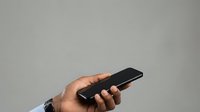 Man holding black smartphone with blank screen against neutral gray background for app mockup and mobile technology concepts.