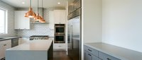 Modern kitchen interior with white cabinets, subway tile backsplash, copper pendant lights, stainless steel appliances and quartz countertops.