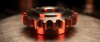 Copper metallic gear wheel component on wooden surface with dramatic lighting for industrial engineering and manufacturing concepts.