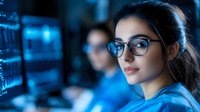 Young female professional in glasses working late at night in modern monitoring center with blue digital screens, focused on data analysis and cybersecurity operations.