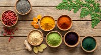 Colorful superfood powders and seeds in wooden bowls on rustic table with moringa leaves and ginger root for healthy nutrition and wellness recipes.
