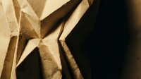 Crumpled brown paper bag texture with dramatic shadows and warm lighting creating abstract geometric patterns and folds for packaging design backgrounds.