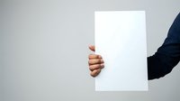 Young adult male with medium brown skin tone holding blank white paper sheet against neutral background, suitable for advertising, marketing mockups, and promotional campaigns.