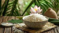 Bowl of steamed jasmine rice on bamboo mat with lotus flower and palm leaves, rustic wooden table setting creates zen atmosphere for spa or dining.
