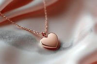 Rose gold heart pendant necklace on soft white silk fabric background with gentle shadows and romantic mood lighting, luxury jewelry macro photography.