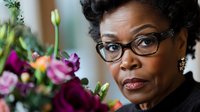 Professional African American businesswoman with glasses and elegant jewelry in office setting with colorful flower arrangement in background.
