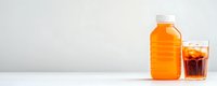 Orange juice bottle and glass filled with ice cubes and dark beverage on white background with copy space, minimalist drink composition.