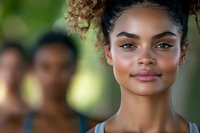 Young African American woman with curly hair smiling confidently outdoors with blurred people in background. Natural beauty portrait for lifestyle content.