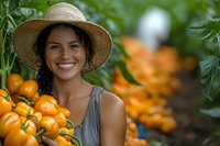 Young Hispanic woman in straw hat smiling while harvesting fresh orange cherry tomatoes in organic garden. Natural summer produce and farming concept.