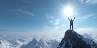 Triumphant climber with arms raised on snowy mountain peak against vast panorama of alpine ranges and bright sunlight in clear blue sky.
