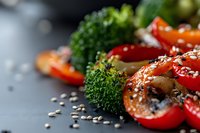 Fresh roasted vegetables with cherry tomatoes, broccoli and sesame seeds on dark background, macro food photography with selective focus and bokeh.
