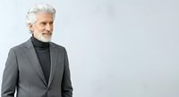 Senior man with white hair and facial hair wearing gray blazer and black turtleneck, isolated on white background for corporate, business, and professional portrait use.