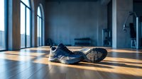 Worn athletic shoe lying on wooden floor in empty industrial loft space with large windows casting dramatic sunlight, suitable for fitness, motivation, and lifestyle concepts.