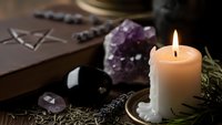 Mystical altar setup with burning candle, amethyst crystal, black obsidian stone and dried herbs for spiritual rituals and meditation practices.
