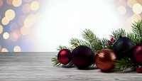 Festive Christmas ornaments in red, copper, and black with pine branches on wooden surface against soft bokeh background.