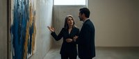 Professional gallery curator woman explaining contemporary artwork to male visitor in modern art museum space during cultural exhibition tour.