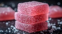 Stack of pink sugar-coated gummy candy squares on dark background with scattered sugar crystals, perfect for food marketing and confectionery advertising.