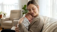 Young Caucasian mother in cozy knit sweater tenderly holding sleeping newborn baby at home, bonding moment in bright living room with natural light.