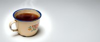 Vintage cream-colored enamel mug with floral design and blue rim filled with hot tea or coffee beverage, isolated on white background for product mockups and design projects.