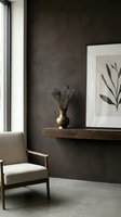 Modern interior with dark textured wall, wooden floating shelf displaying brass vase with dried flowers, framed botanical art, and beige upholstered chair by window for home decor.