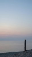 Serene coastal scene with wooden post on sandy beach during twilight hour with pastel sky colors reflecting on calm ocean water for peaceful meditation.