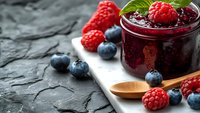 Homemade berry jam with fresh raspberries and blueberries on rustic wooden board. Organic fruit preserve for breakfast, desserts and healthy eating concepts.