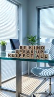 Wooden letter blocks spelling BE KIND SPEAK UP RESPECT ALL on modern glass desk in bright office with venetian blinds creating shadow patterns.