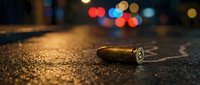 Bullet casing on wet asphalt street at night with colorful bokeh lights creating dramatic crime scene atmosphere for forensic investigation concepts.
