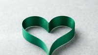 Green satin ribbon twisted into heart shape on white background. Romantic symbol for Valentine's Day, wedding decoration, love concept, gift wrapping.