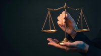 Hand holding golden scales of justice against dark background symbolizing legal balance, law firm services, attorney consultation, and judicial fairness concepts.