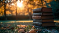 Stack of vintage books on autumn grass with golden sunset light filtering through trees in background, creating nostalgic outdoor reading atmosphere.