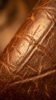 Close-up macro shot of brown leather texture with detailed stitching and natural grain patterns in warm golden lighting for luxury fashion design.