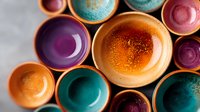 Colorful ceramic bowls and plates in vibrant orange, purple, turquoise and pink tones arranged in artistic composition, shot from above with soft natural lighting.